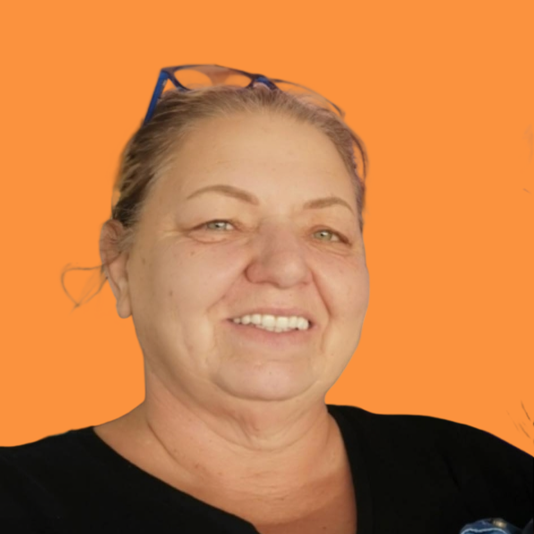 Woman with glasses on head smiles at camera, wearing a black shirt, orange background.