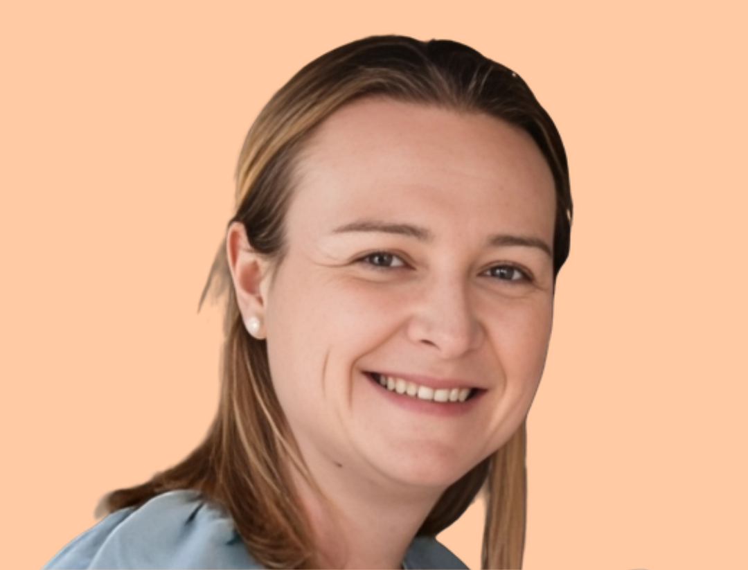 Woman with blonde hair smiles at camera, wearing a blue shirt. Peach background.