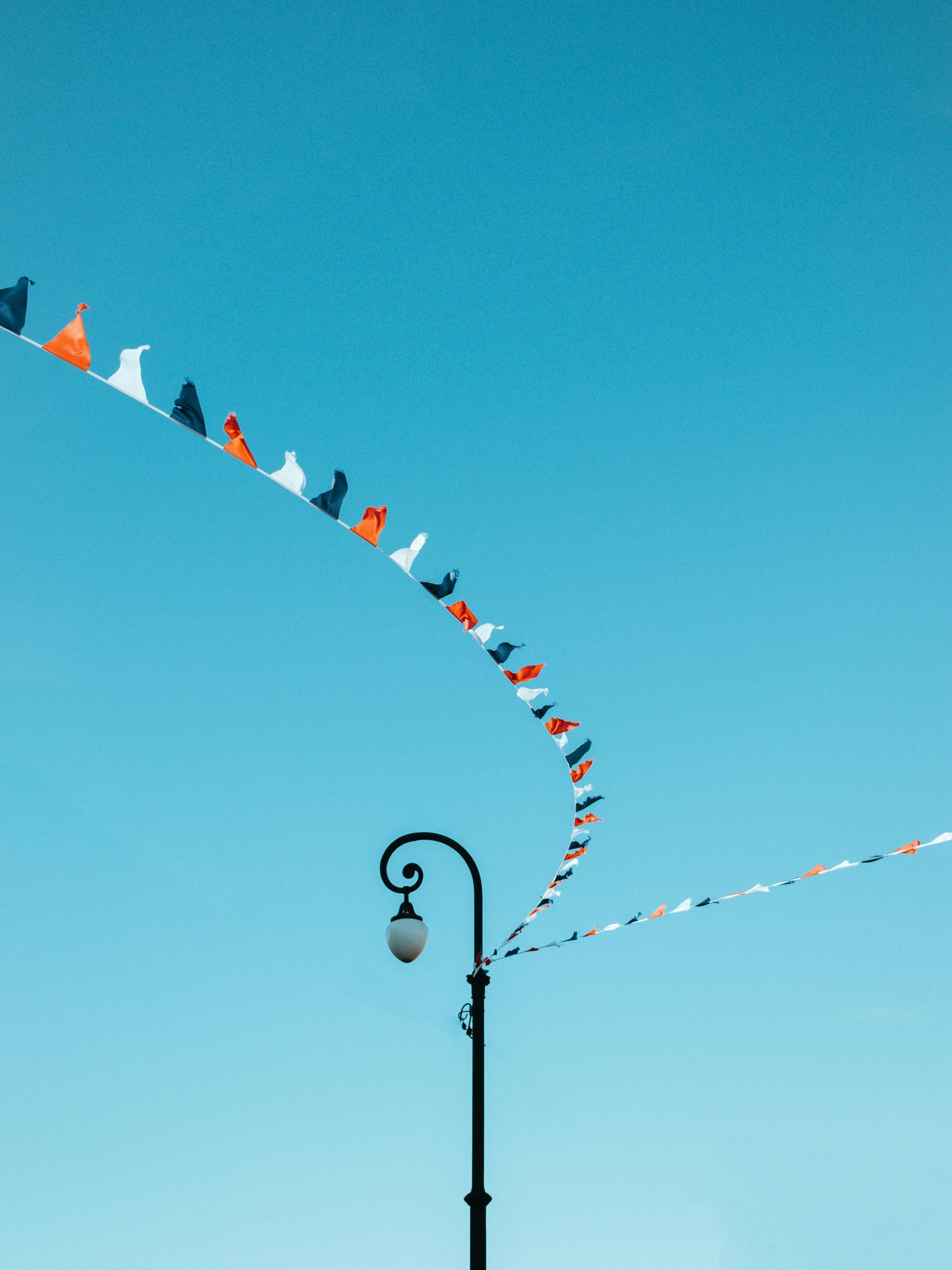 Lamp post with colorful pennant flags against a bright blue sky.