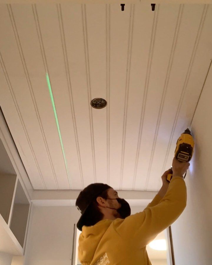 A man in a yellow hoodie is using a drill on a wall