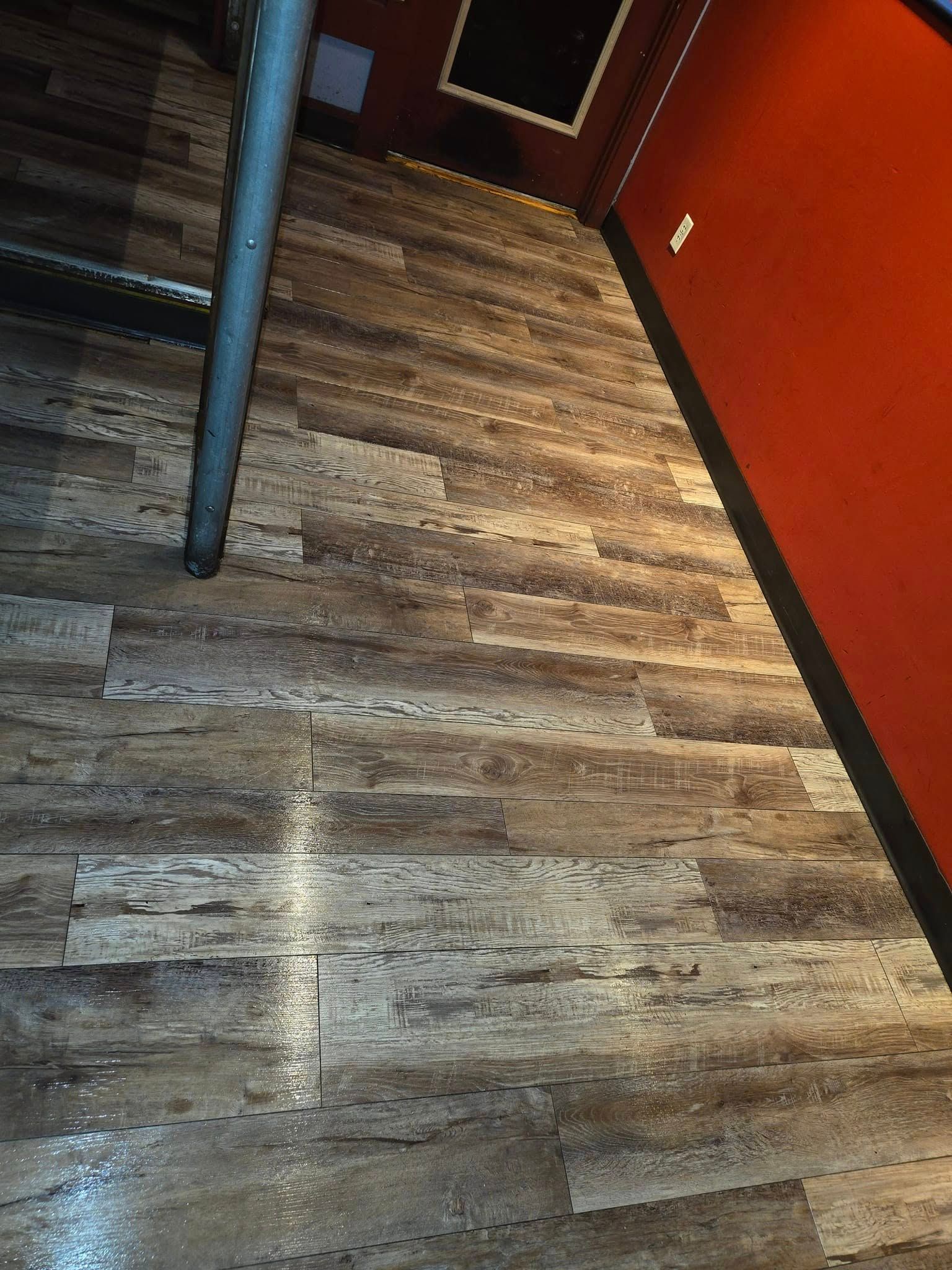 A wooden floor in a room with stairs and a red wall.