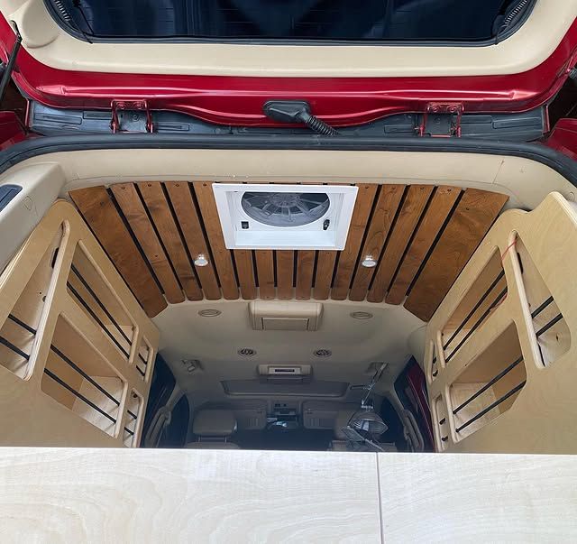 The trunk of a red van with wooden shelves and a fan.