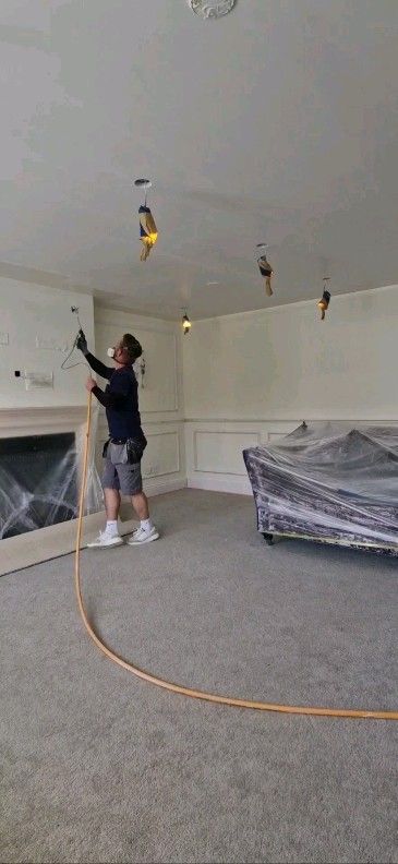 A man is working on the ceiling of a living room.