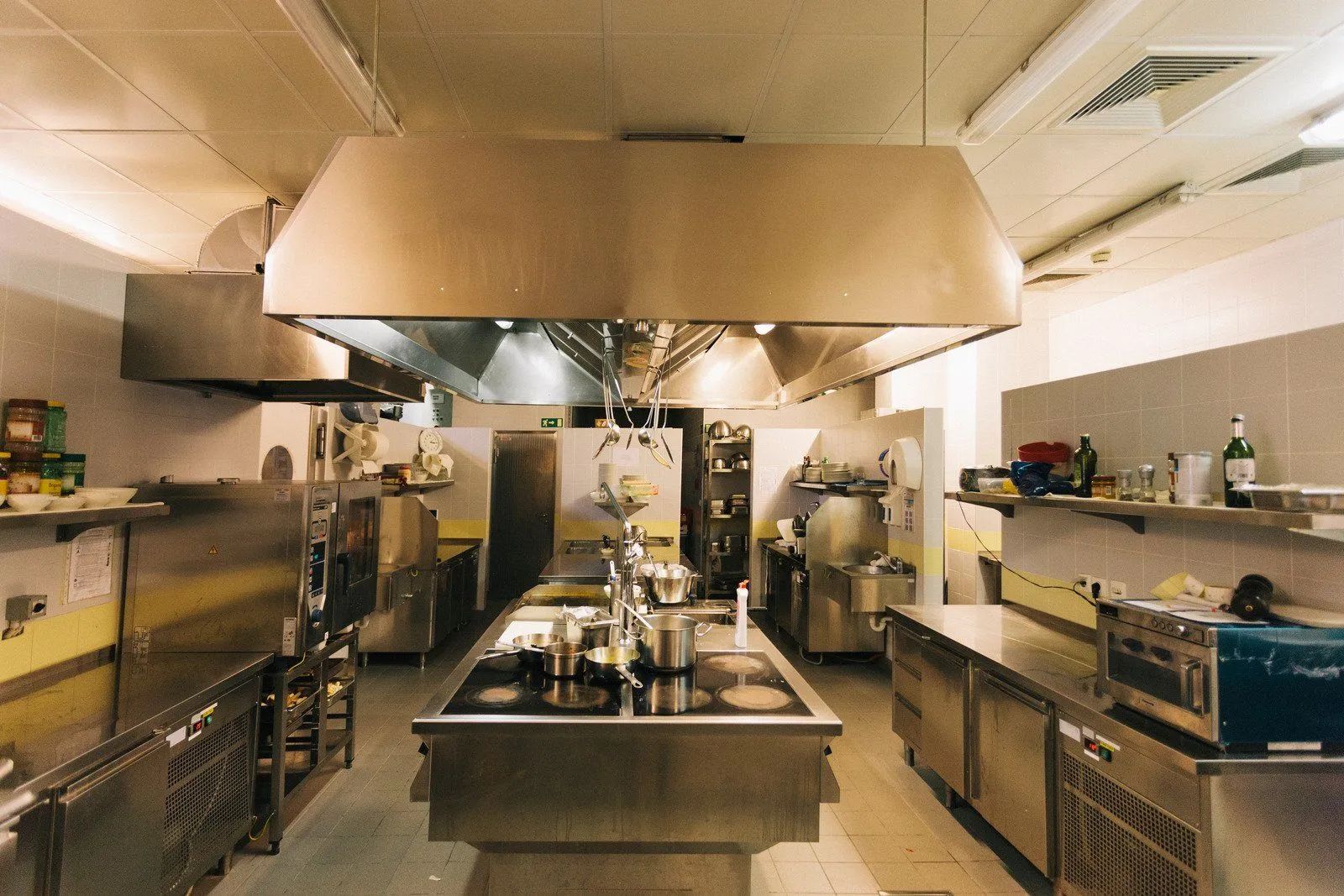 Commercial kitchen with stainless steel appliances and ventilation hoods.