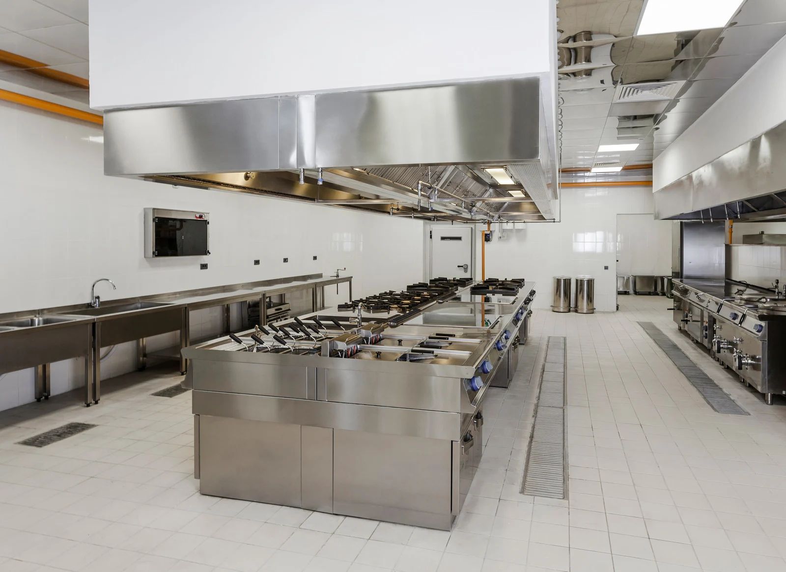 A spacious, clean commercial kitchen featuring stainless steel cooking ranges, prep counters, and overhead ventilation.