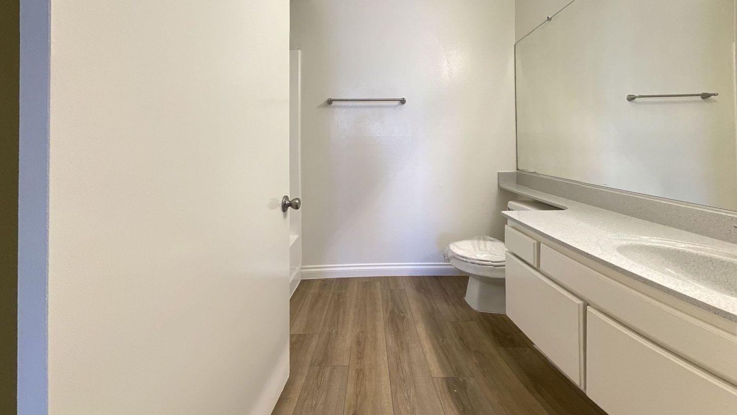 Bathroom with white vanity, toilet, and towel rack; light wood-look flooring.