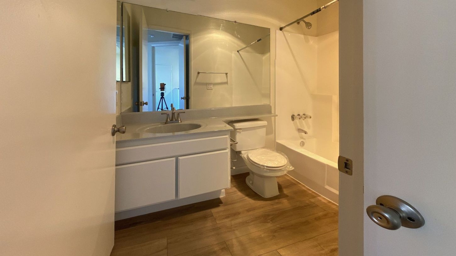 Bathroom with white vanity, toilet, and shower/tub. Beige wood-look flooring.