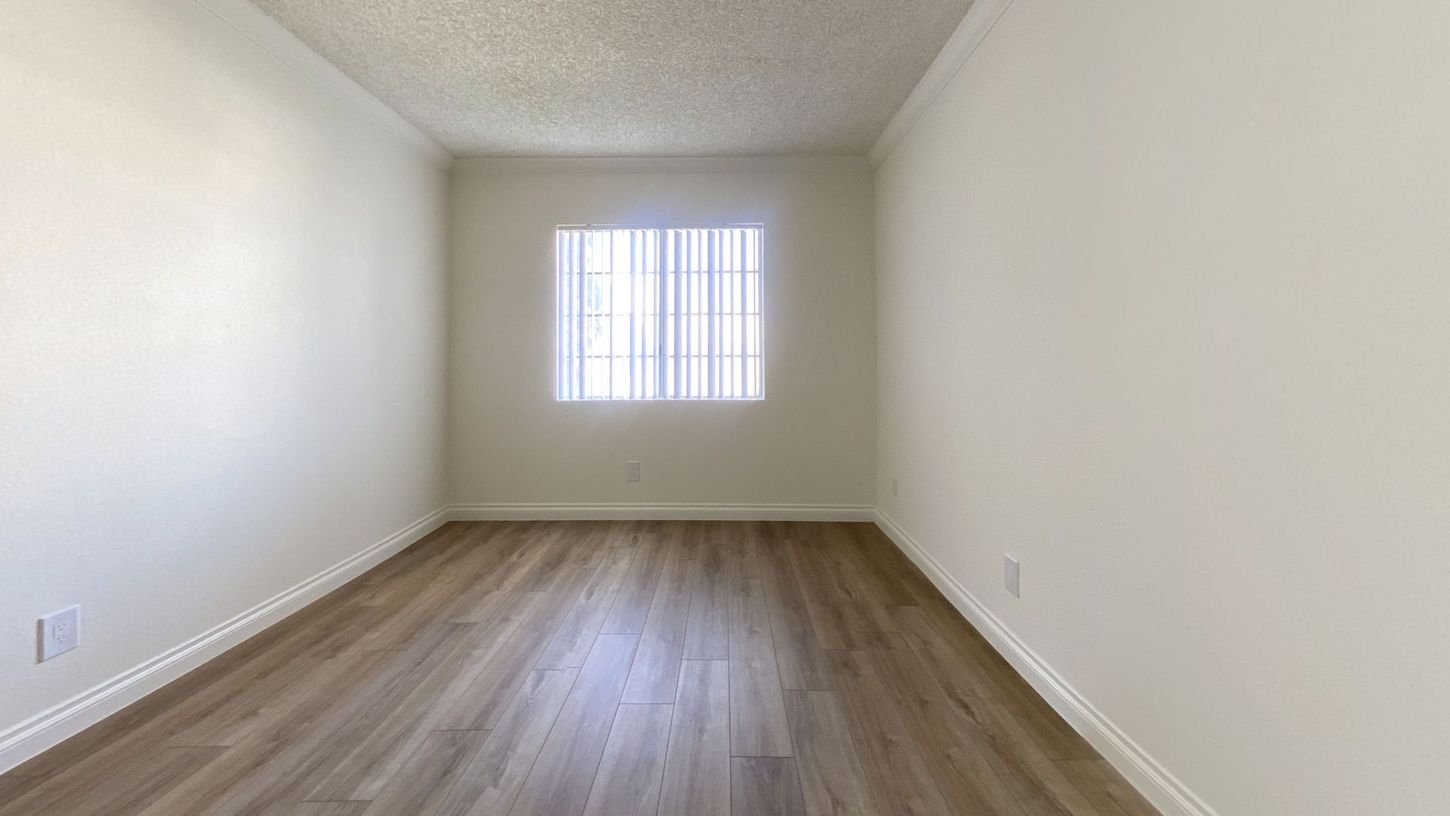 Empty room with white walls, window, and wood-look flooring.