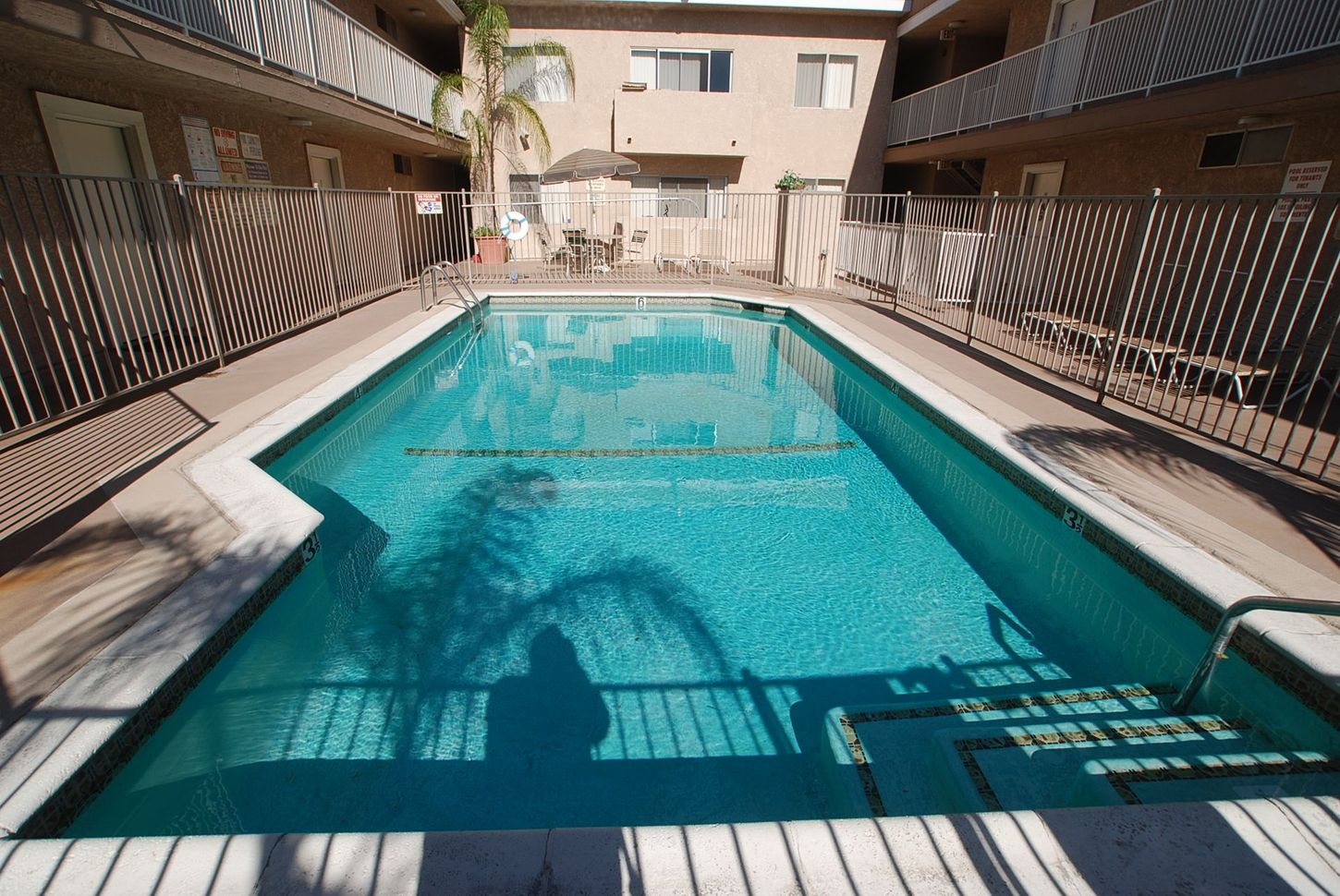 A rectangular outdoor swimming pool surrounded by a fence and apartment buildings.