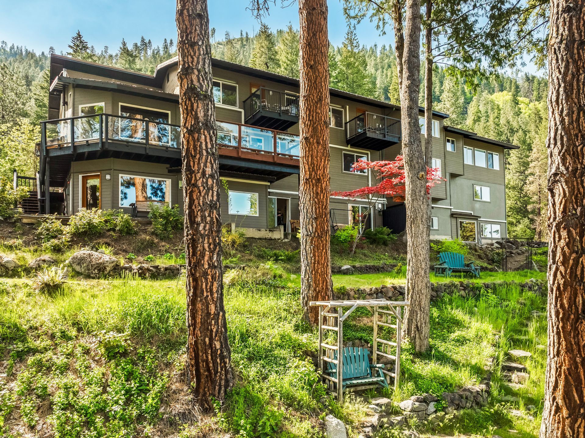 Multi-story house nestled in a forest, featuring balconies, windows, and a lush green landscape.