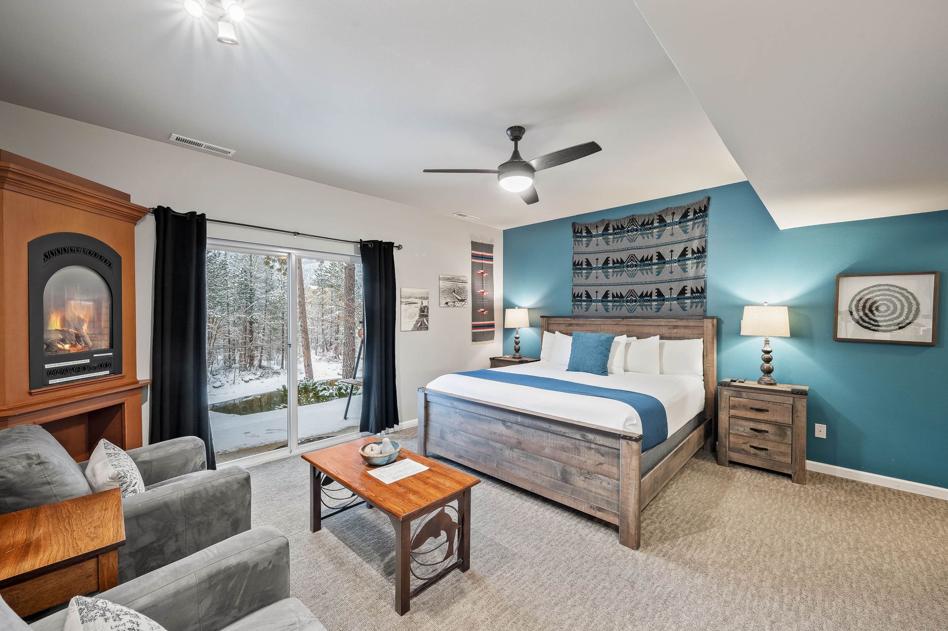 Bedroom with bed, fireplace, and sliding door to snowy outdoors. Teal accent wall, gray furniture.