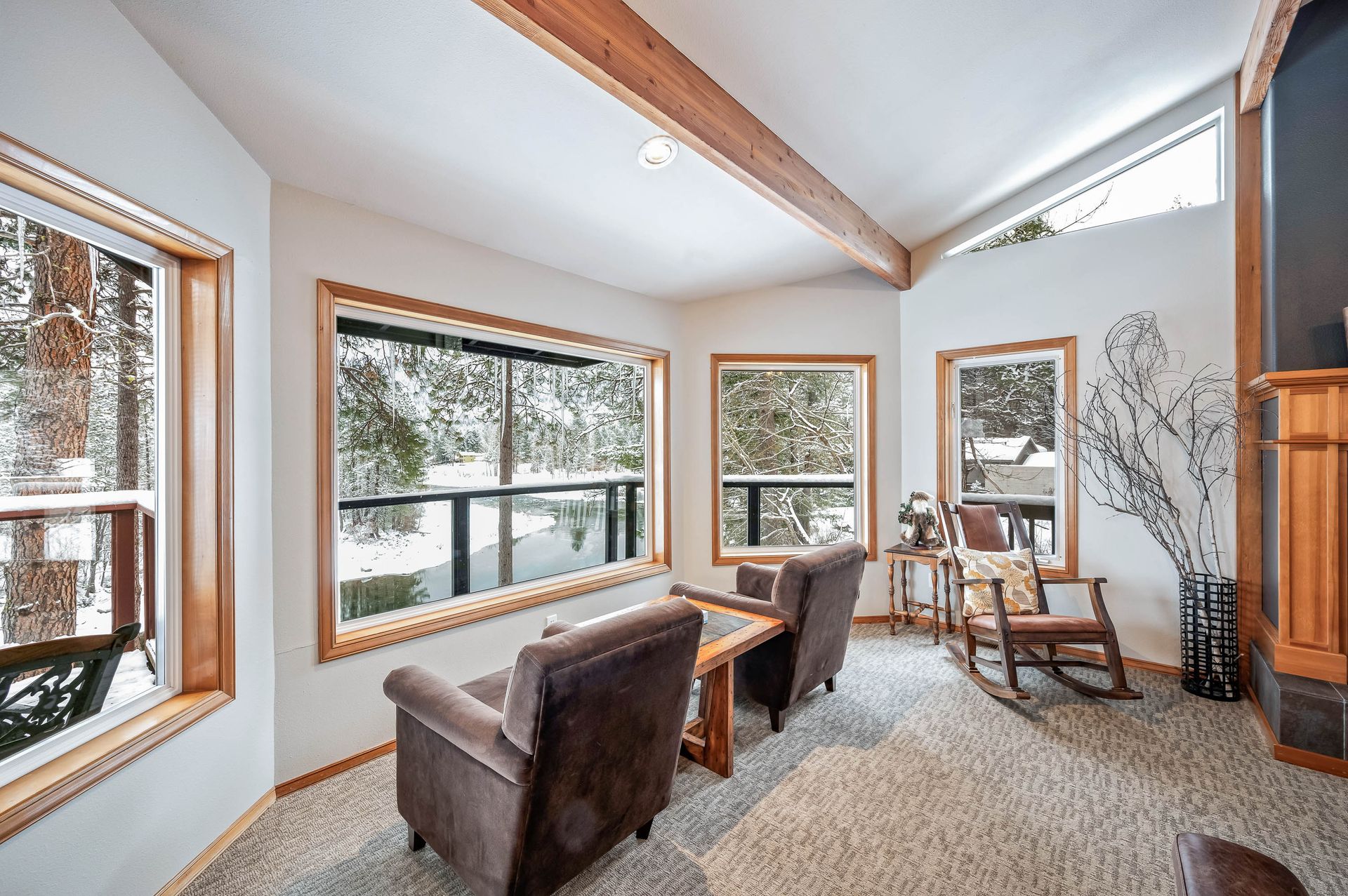 Living room with brown armchairs, windows overlooking a snowy scene, and exposed wooden beams.
