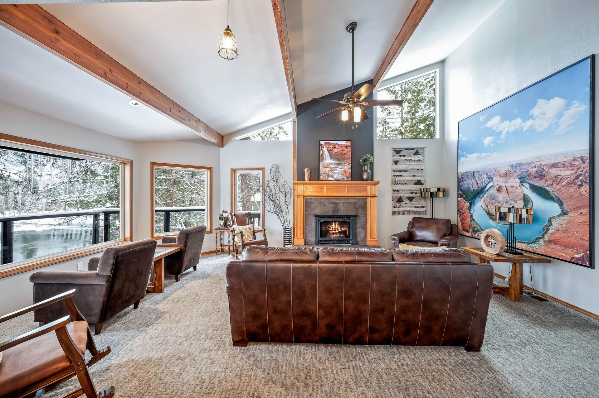 Living room with leather furniture, fireplace, large landscape artwork, and snow-covered view.