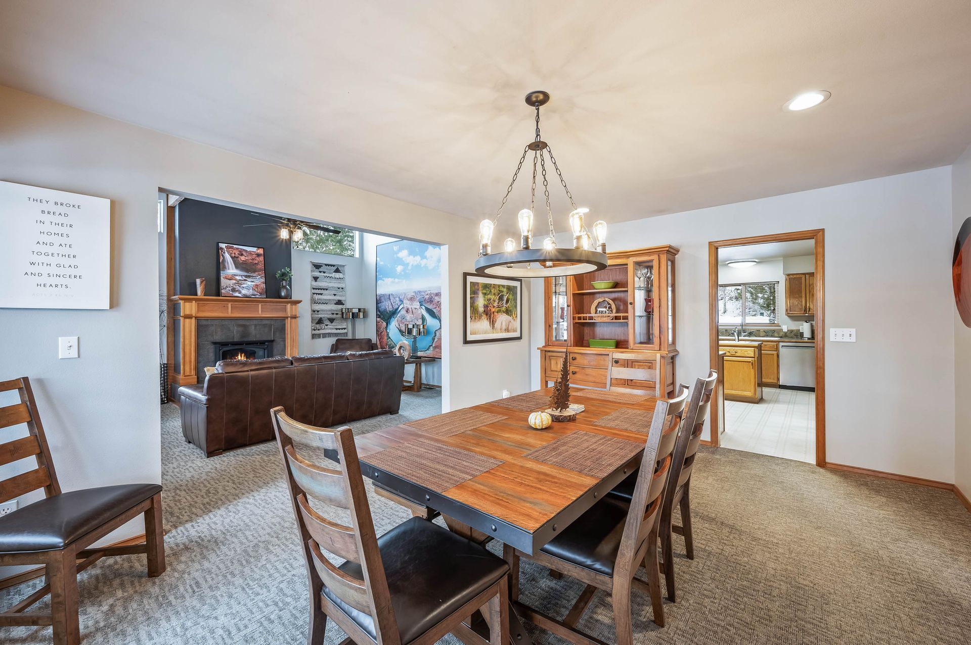 Dining room with wooden table, chairs, chandelier, open to living room with fireplace and kitchen.