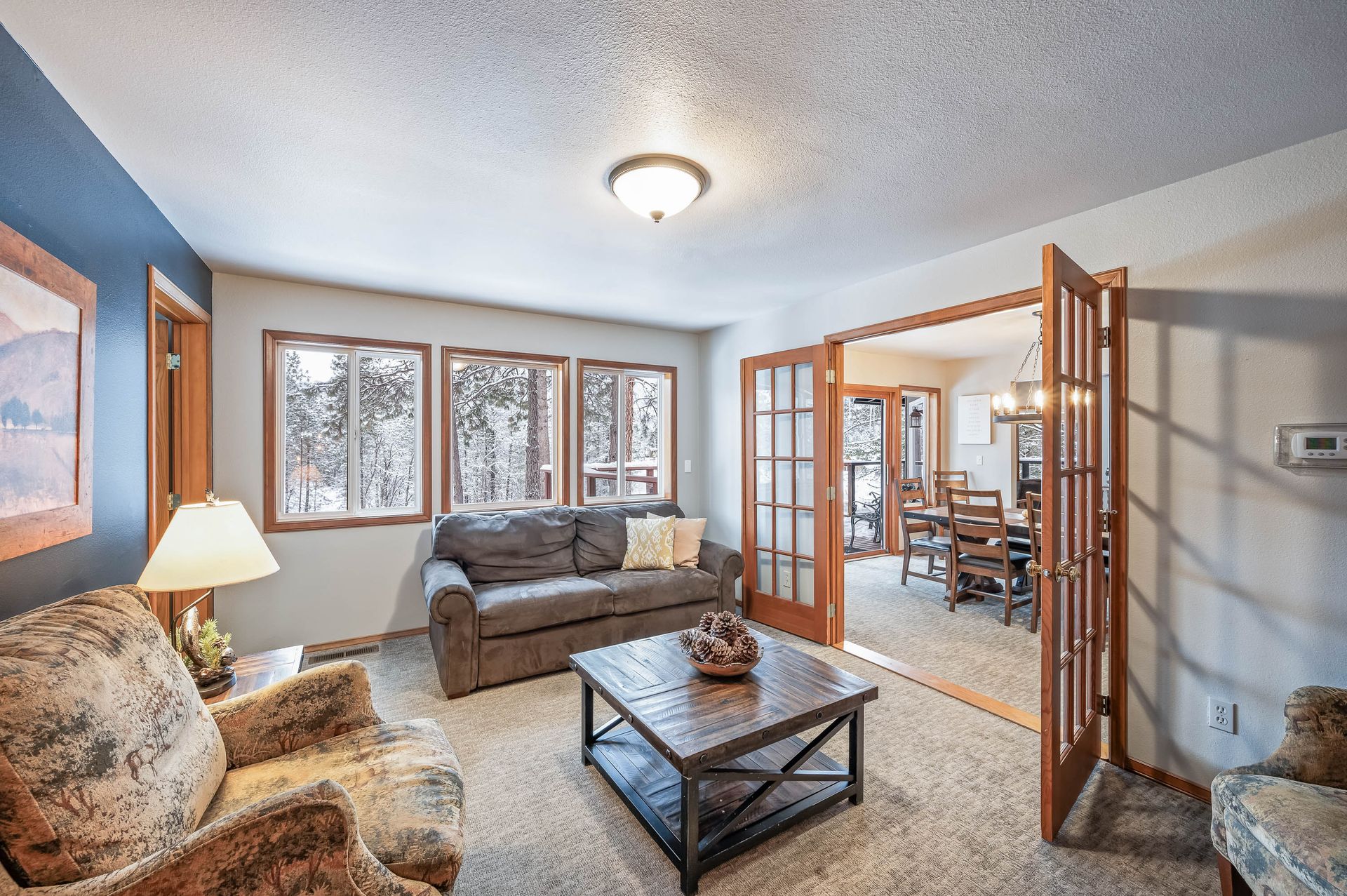 Living room with gray sofa, windows looking to snowy landscape, and French doors to dining area.