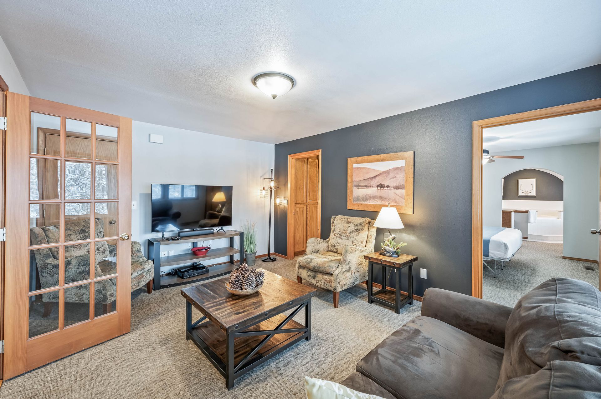 Living room with seating, TV, and French doors; gray accent wall, beige carpet, neutral tones.
