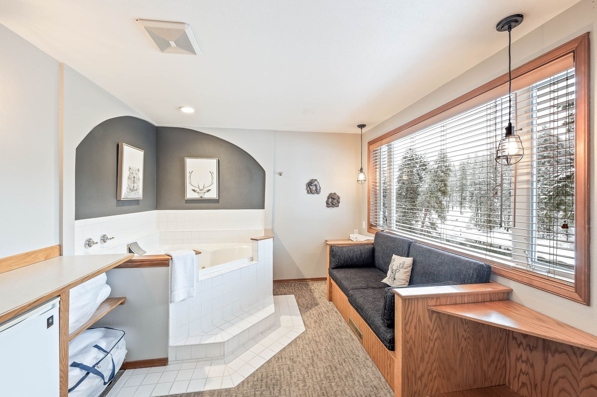 Cozy hotel room with a jacuzzi, sofa, and window overlooking a snowy scene.