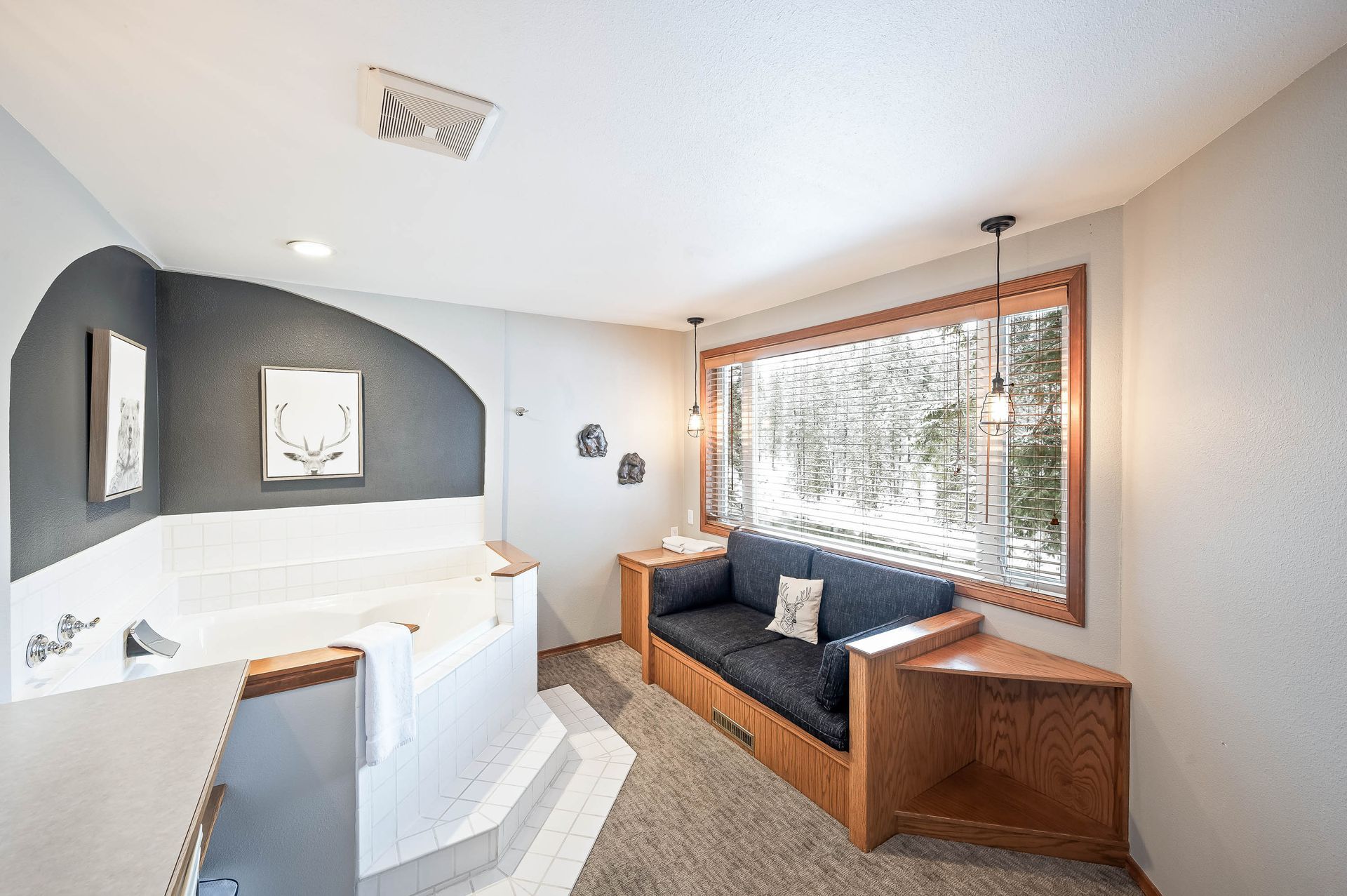 Cozy bathroom with a jacuzzi, built-in sofa by a window, and artwork. Neutral colors, natural light.