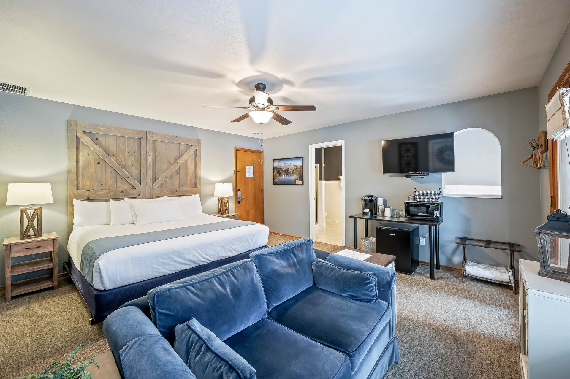 Hotel room with king bed, blue sofa, desk with coffee station, and TV.