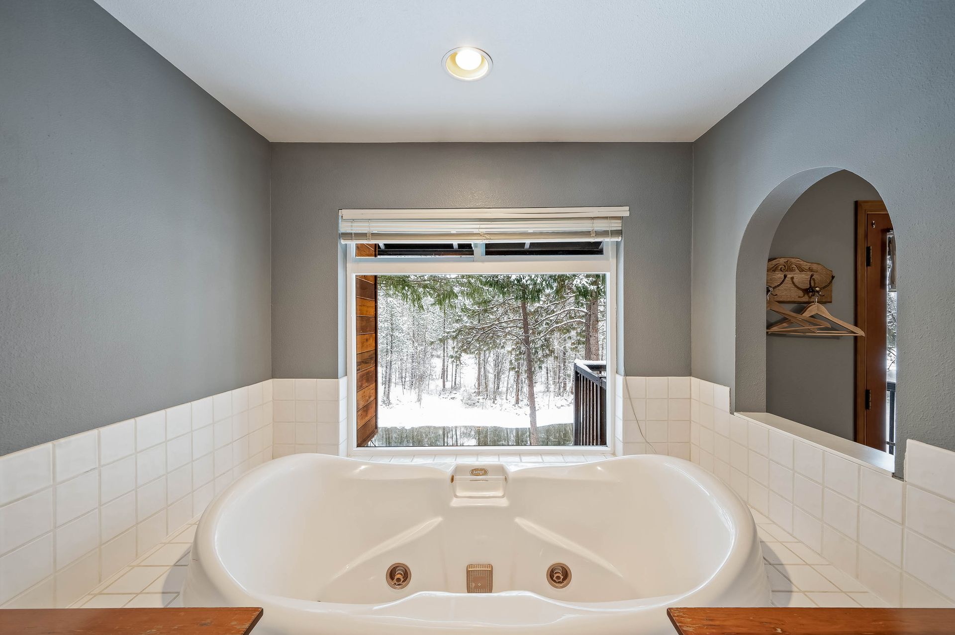 Bathroom with a white jacuzzi tub, window overlooking snowy trees, and gray walls.