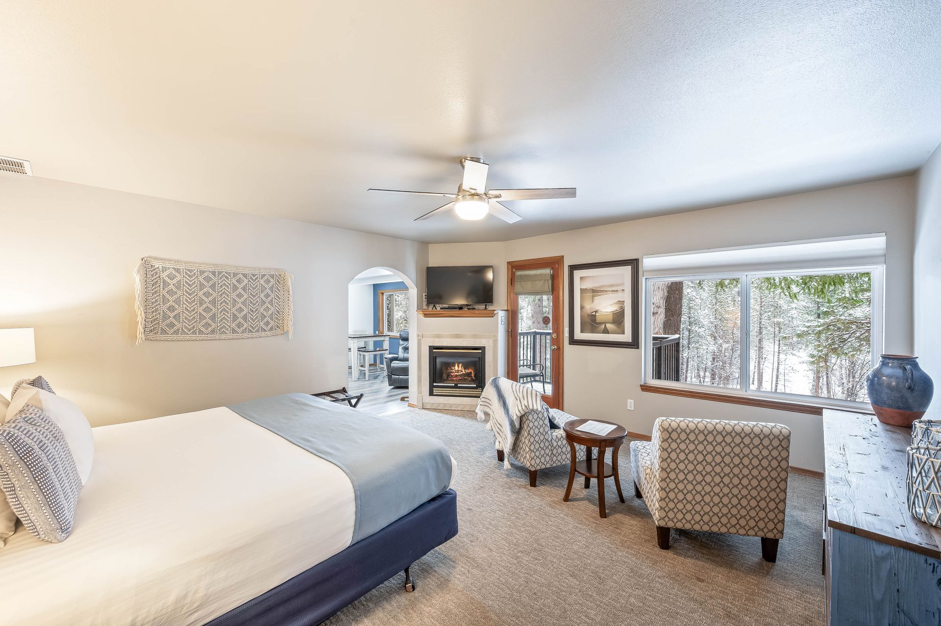 Bedroom with a king-sized bed, fireplace, chairs, and window overlooking a snowy landscape.