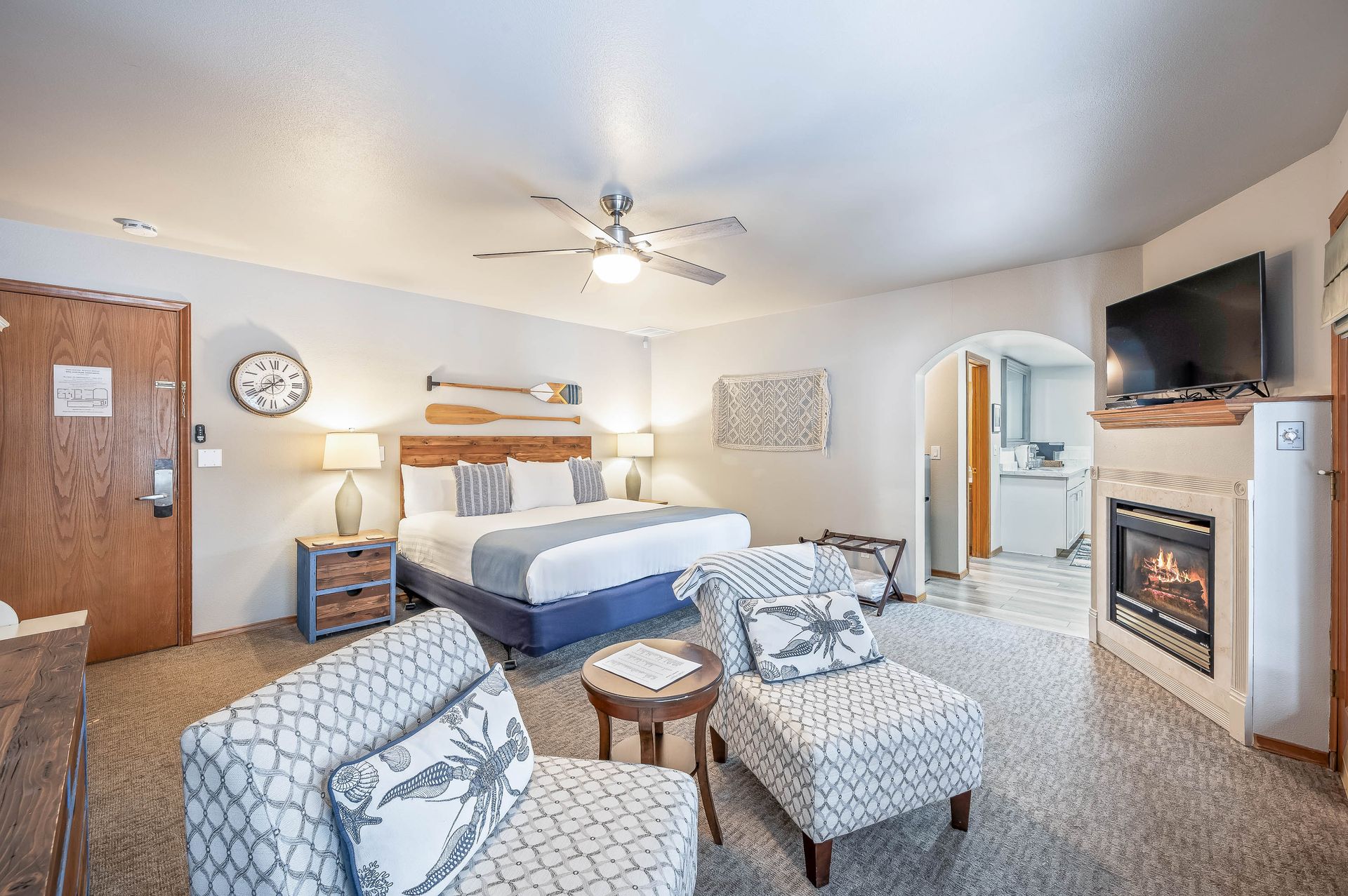 Hotel room with a king bed, fireplace, two armchairs, and a small round table.