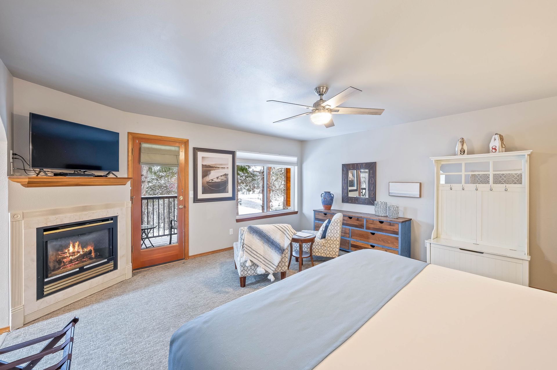 Bedroom with fireplace, balcony, windows, beige carpet, and a large bed with a light blue blanket.