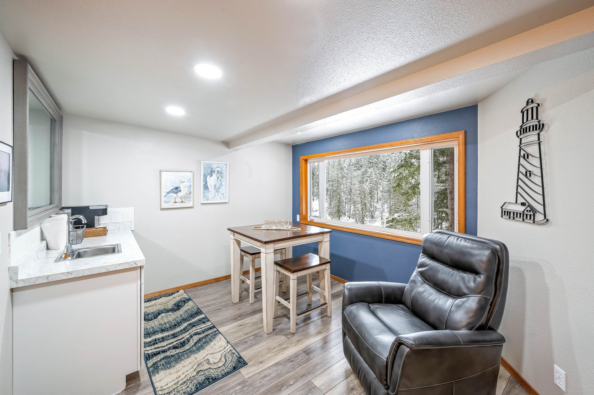 Interior with small dining table, recliner, sink, and window overlooking snowy trees.
