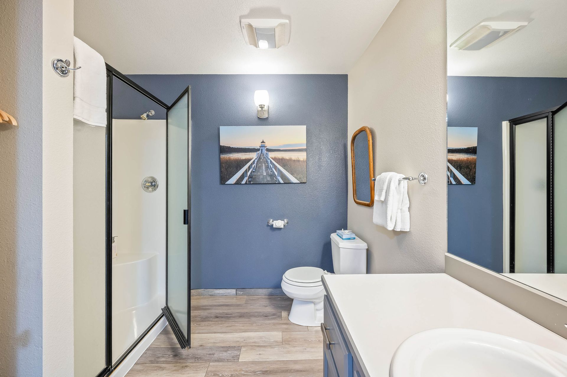 Bathroom with blue accent wall, glass shower, toilet, sink, mirror, and artwork.