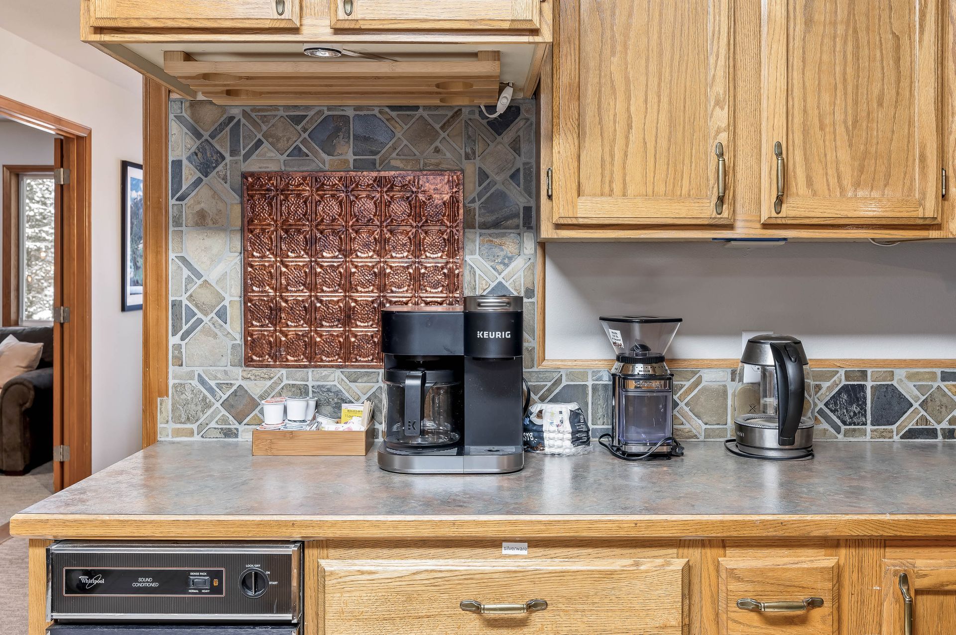 Kitchen counter with coffee maker, grinder, and kettle under wooden cabinets.