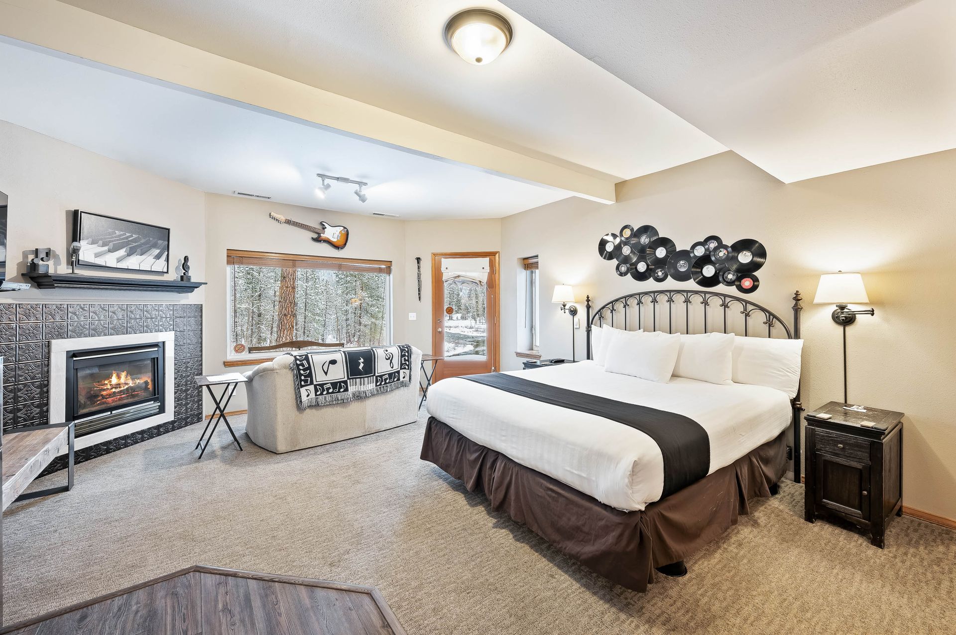 Cozy bedroom with fireplace, bed, and sitting area; view of snow-covered trees outside window.