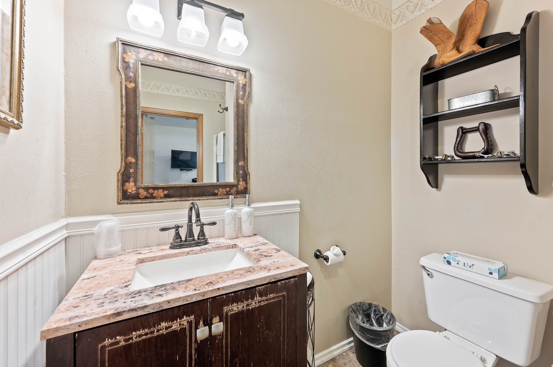 Bathroom with vanity, mirror, toilet, and shelving with decorations.