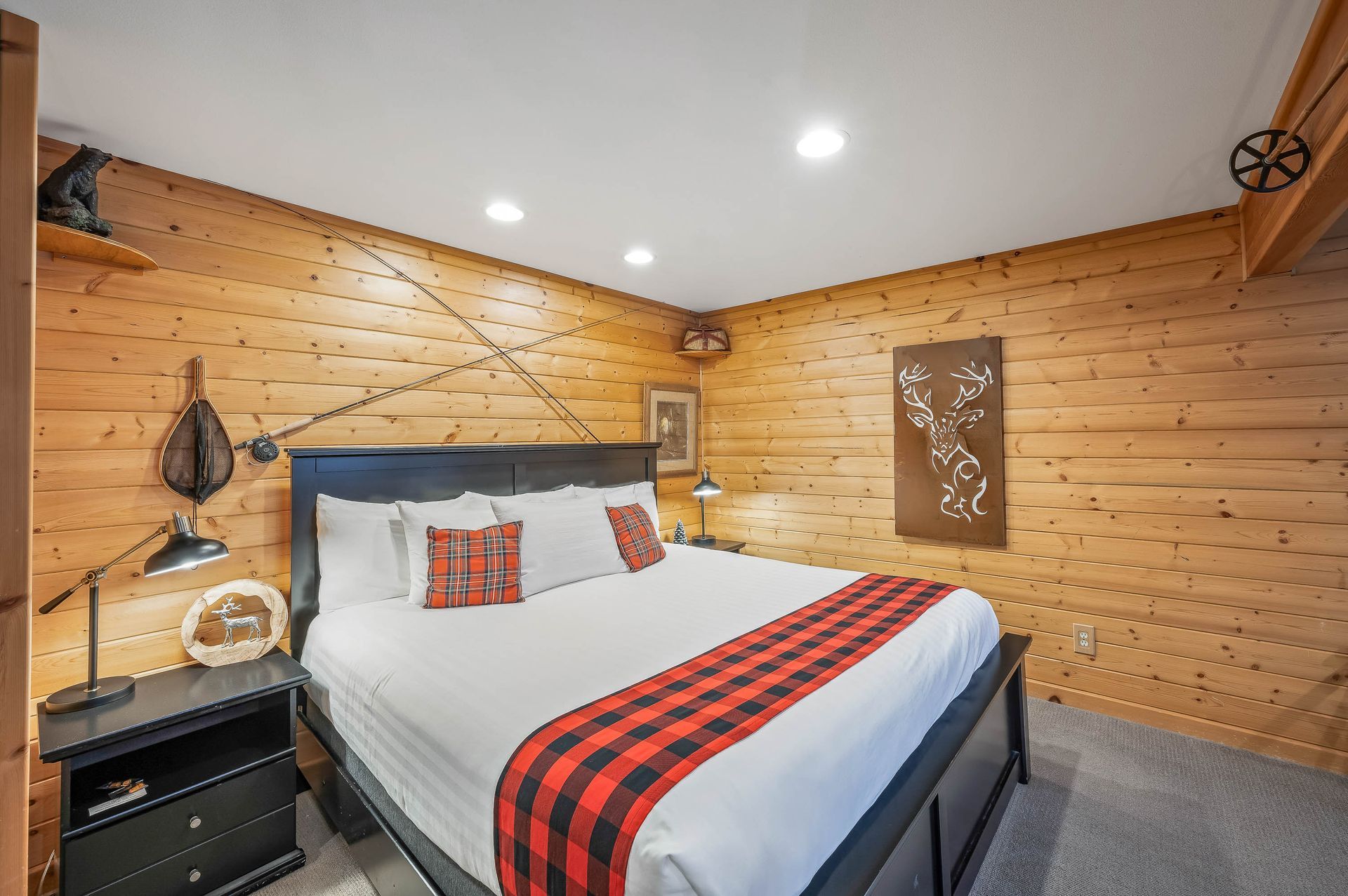 Bedroom with wood paneling, black bed, red plaid accents, nightstand with lamp.