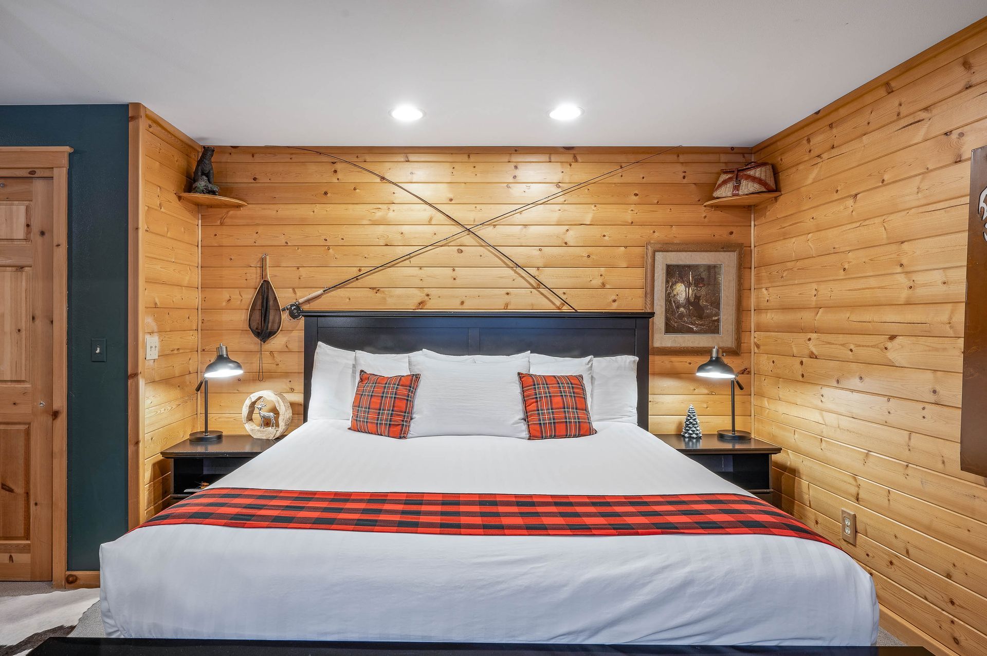 Bedroom with wood-paneled walls, a large bed with red plaid accents, and two nightstands with lamps.
