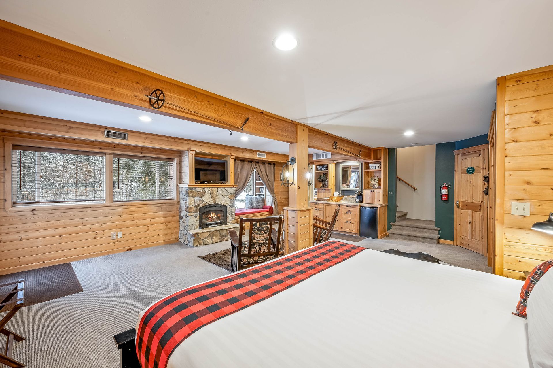 Rustic cabin bedroom with fireplace, window, bed, wood paneling, and a small bar area.