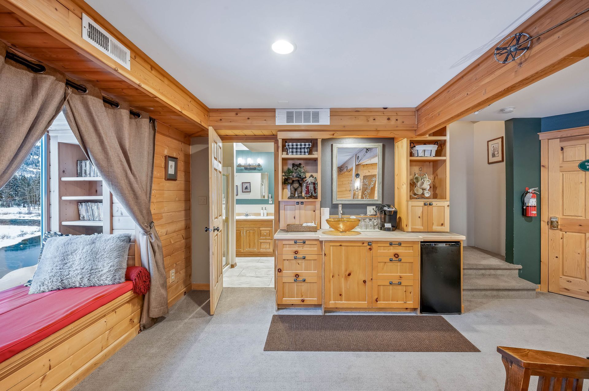 Cozy cabin interior with wood paneling, built-in bar, and window seat overlooking snow.