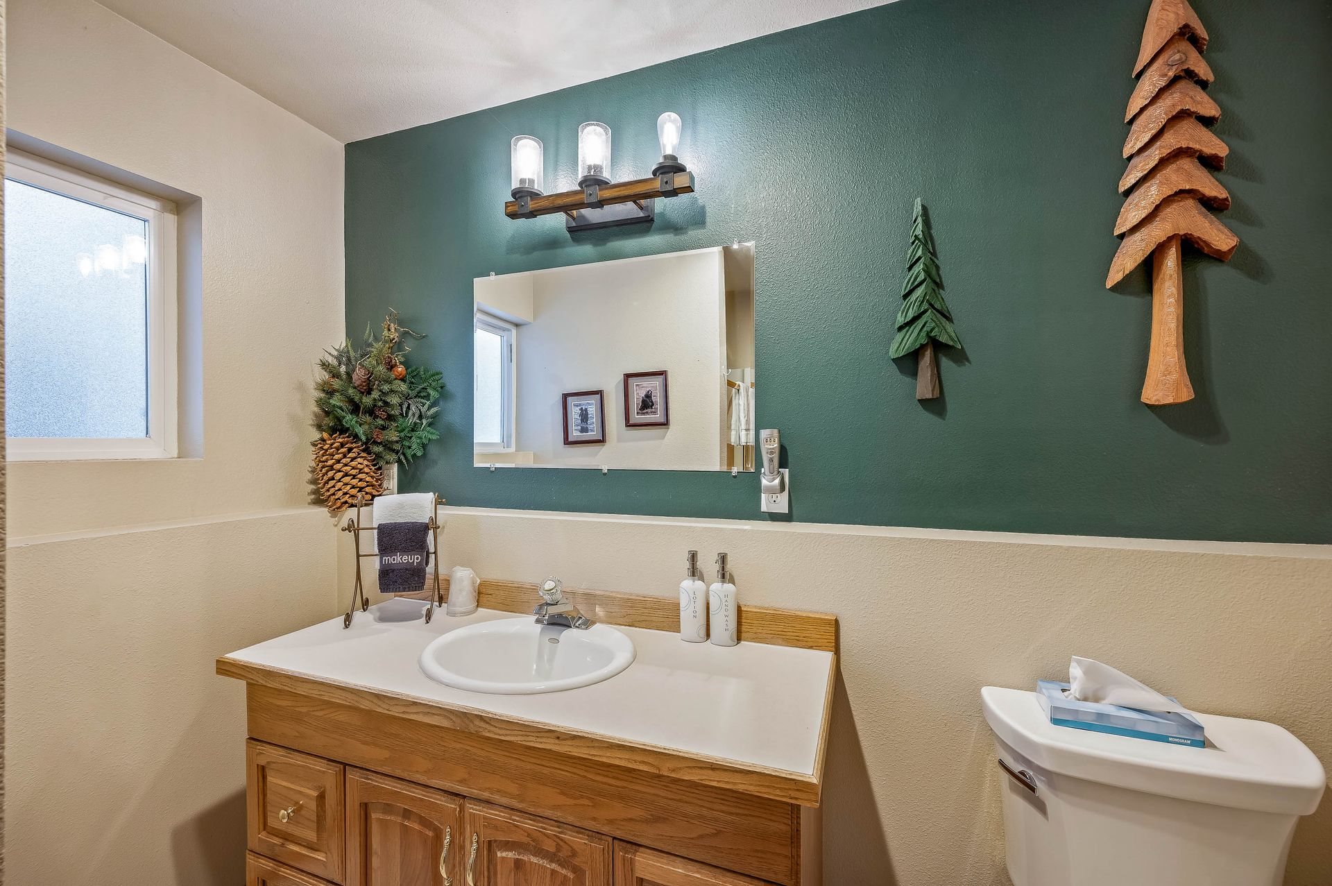 Rustic bathroom with green accent wall, wooden vanity, and pine tree decor.