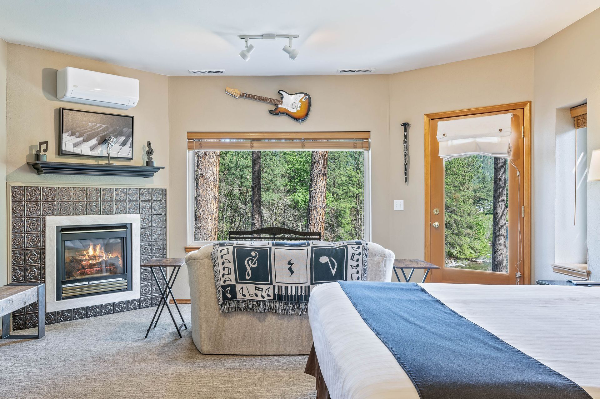 Cozy bedroom with fireplace, couch, guitar, and window overlooking trees.