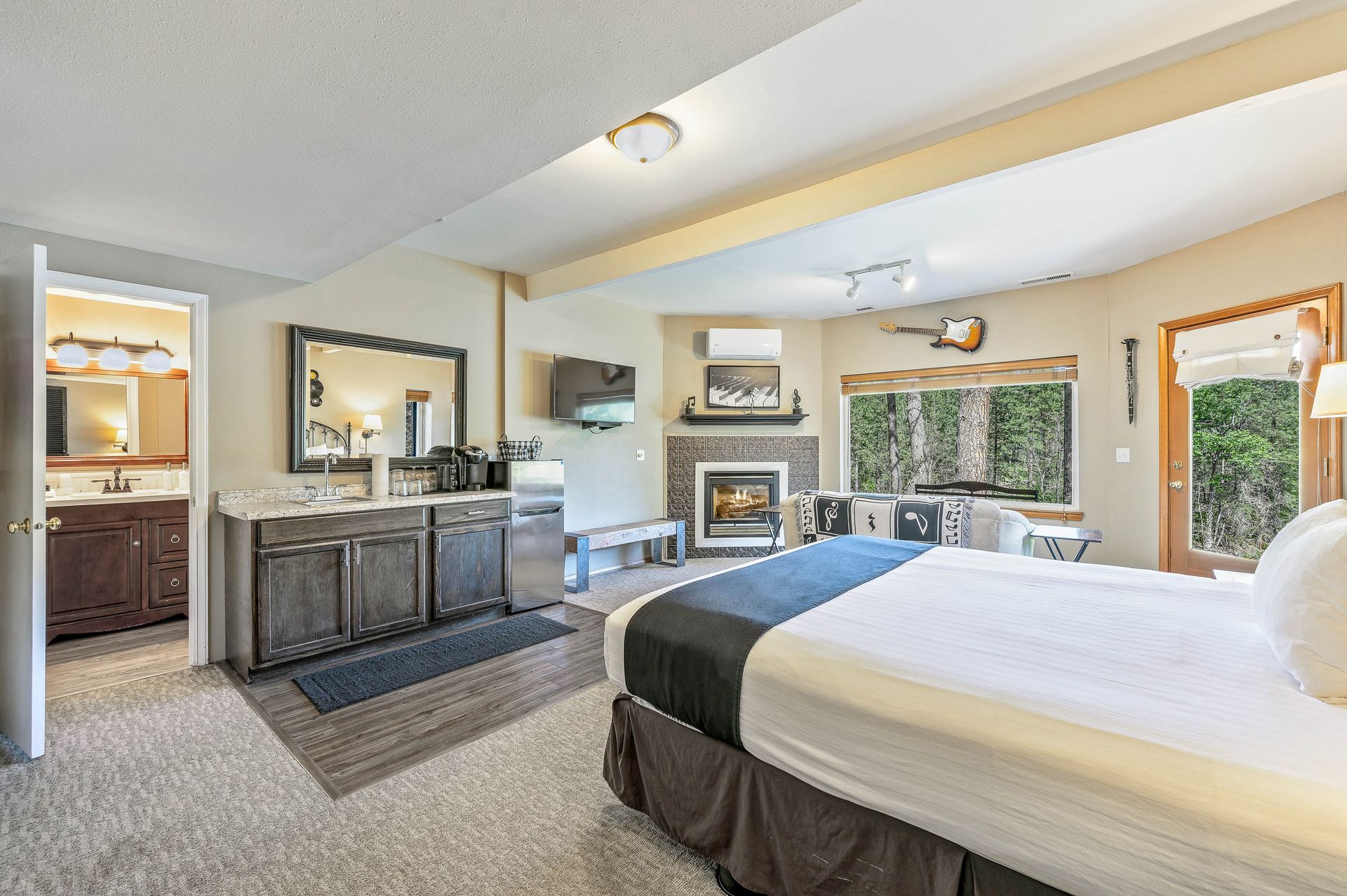 Bedroom with king bed, fireplace, kitchenette, and view of trees through a window.