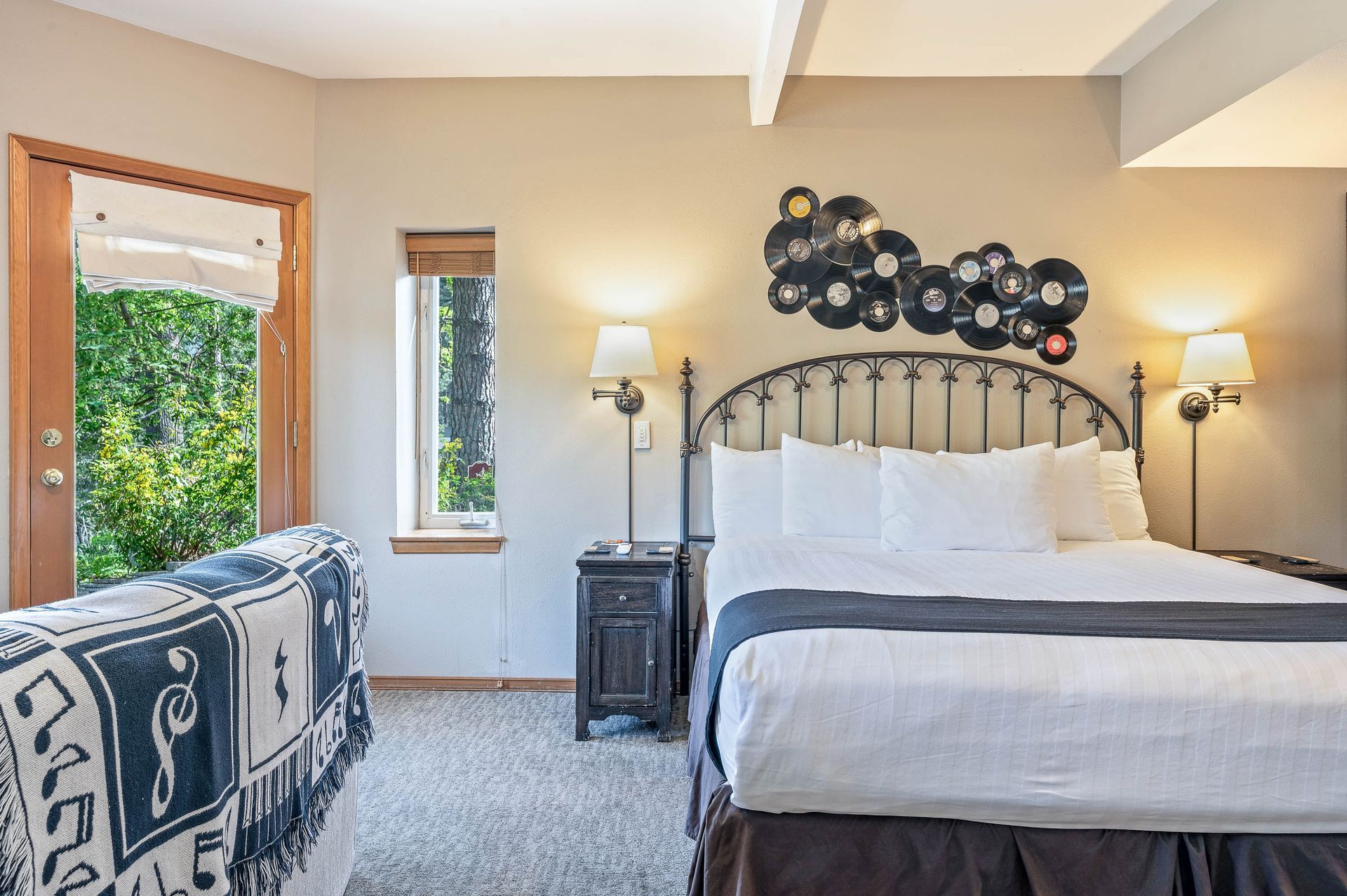 Bedroom with bed, records wall art, open door to trees, and small couch with musical blanket.