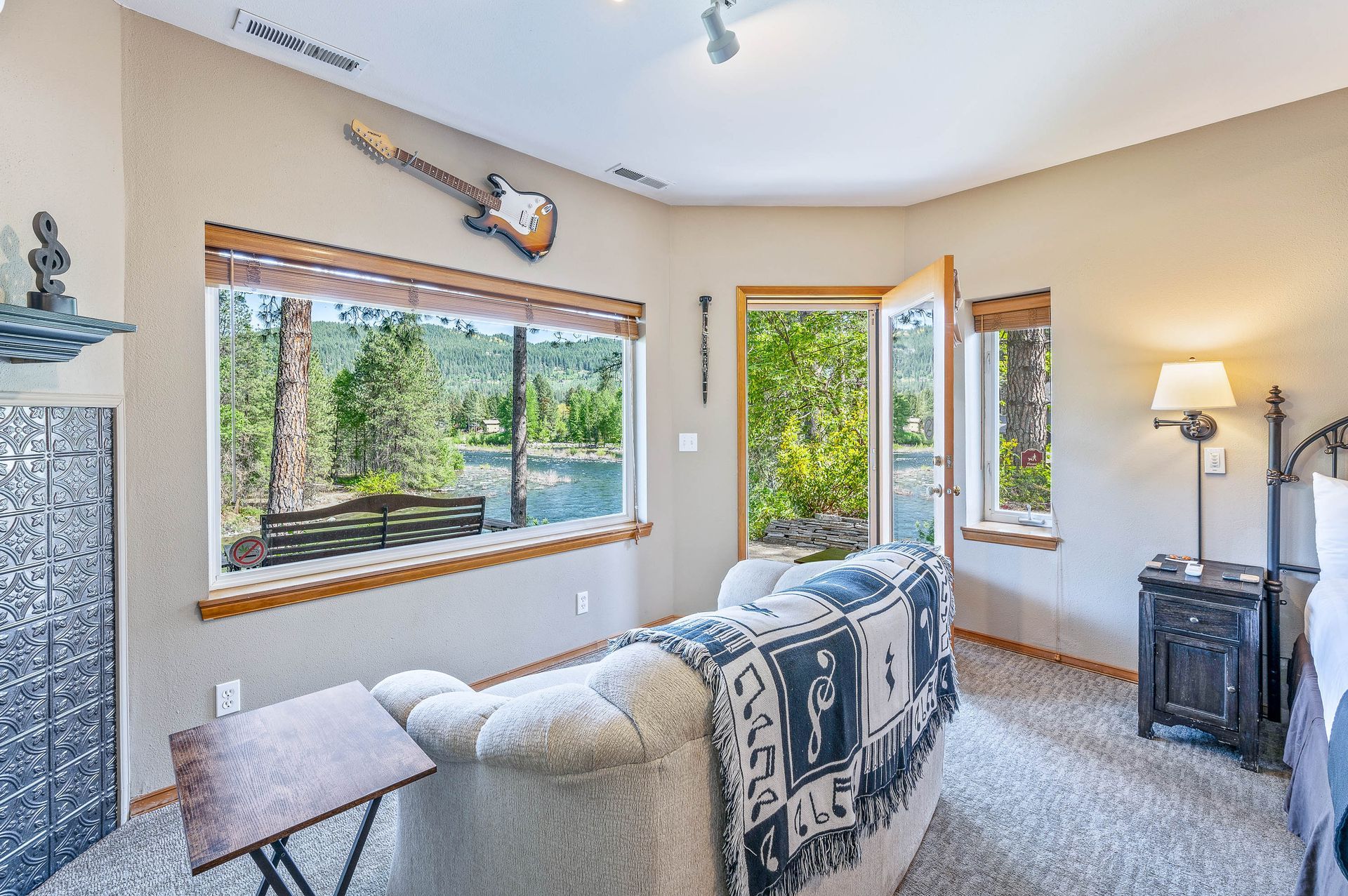 Bedroom with sofa, guitar, large window, and door overlooking a wooded area.