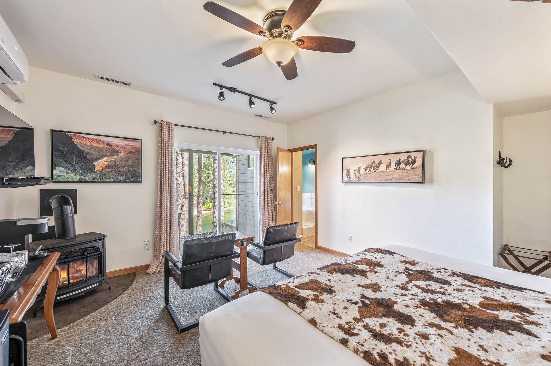 Bedroom with fireplace, bed with cowhide blanket, chairs, and sliding door to trees.