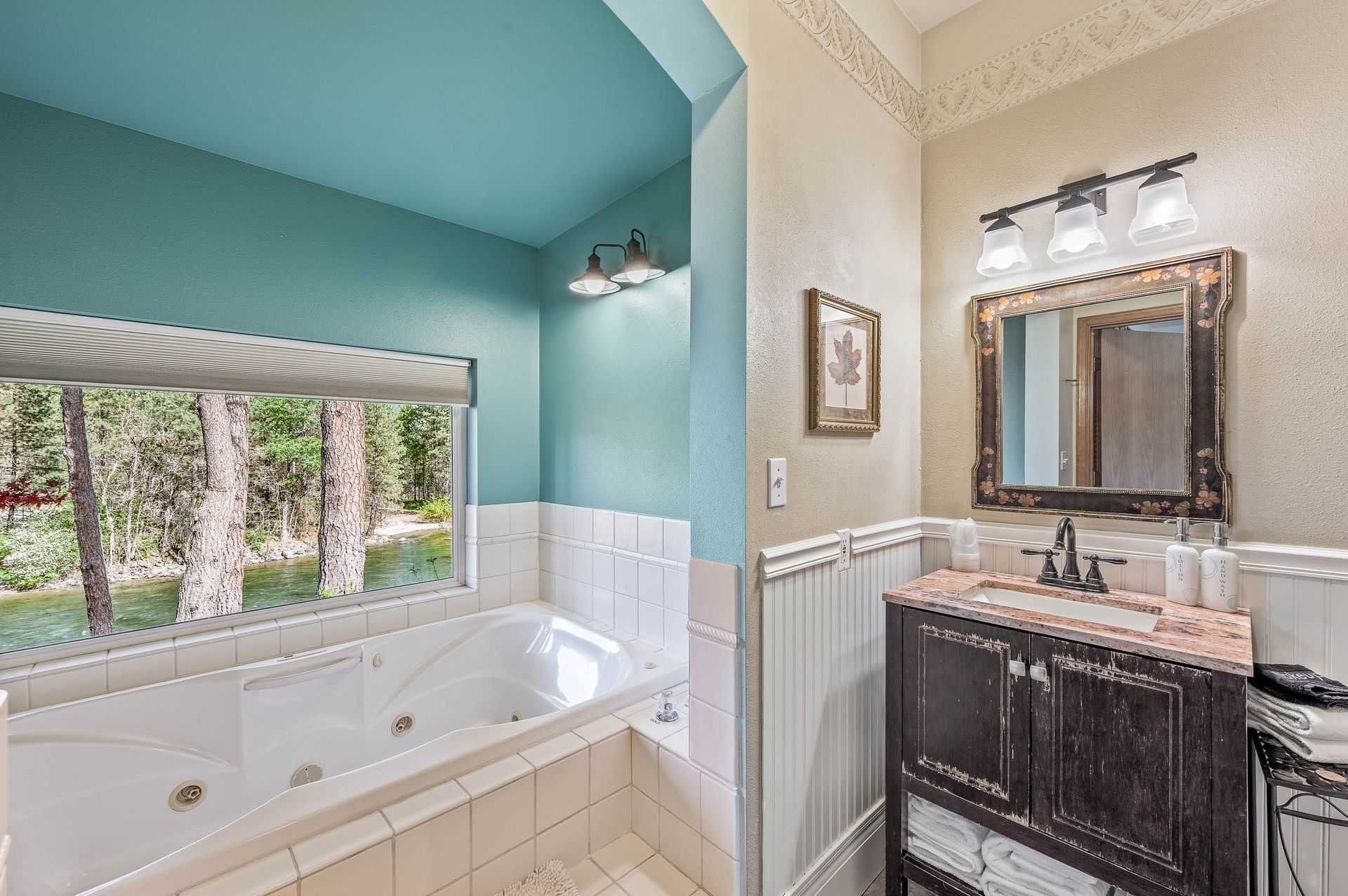 Bathroom with jacuzzi tub, vanity, and window overlooking trees; turquoise walls and ceiling.
