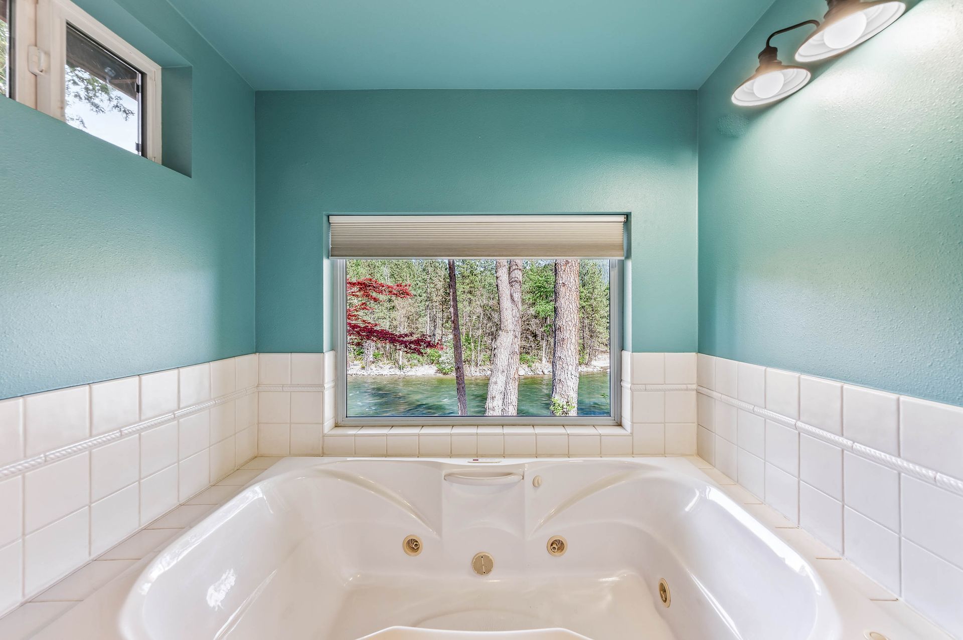 A white jacuzzi tub in a bathroom with turquoise walls and a window overlooking trees.