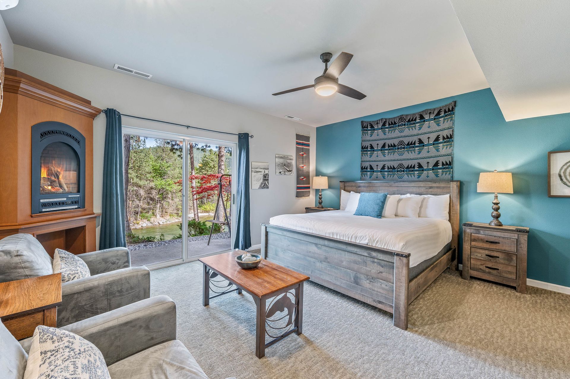 Spacious bedroom with king bed, fireplace, and sliding glass door leading to a patio with lush greenery.
