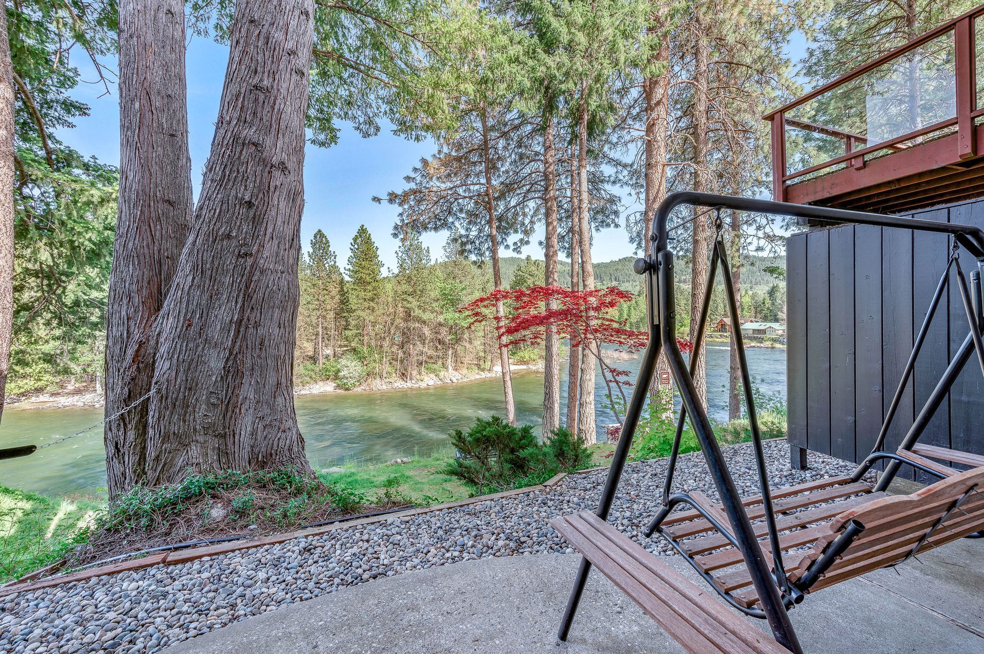 Swing set on a patio overlooking a river. Trees and foliage frame the view.