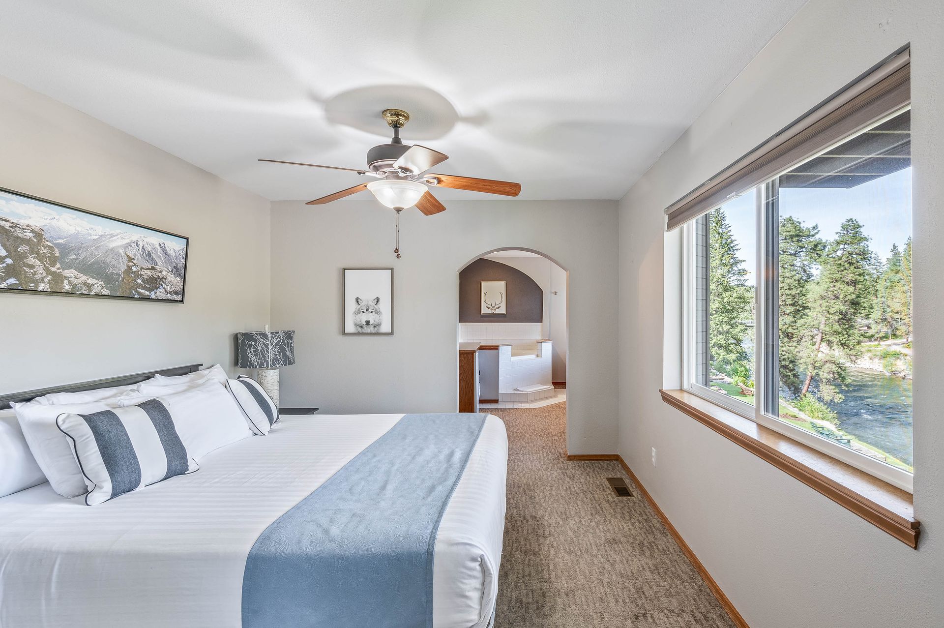Bedroom with king bed, window, and view of trees. Neutral color scheme, ceiling fan, archway to bathroom.