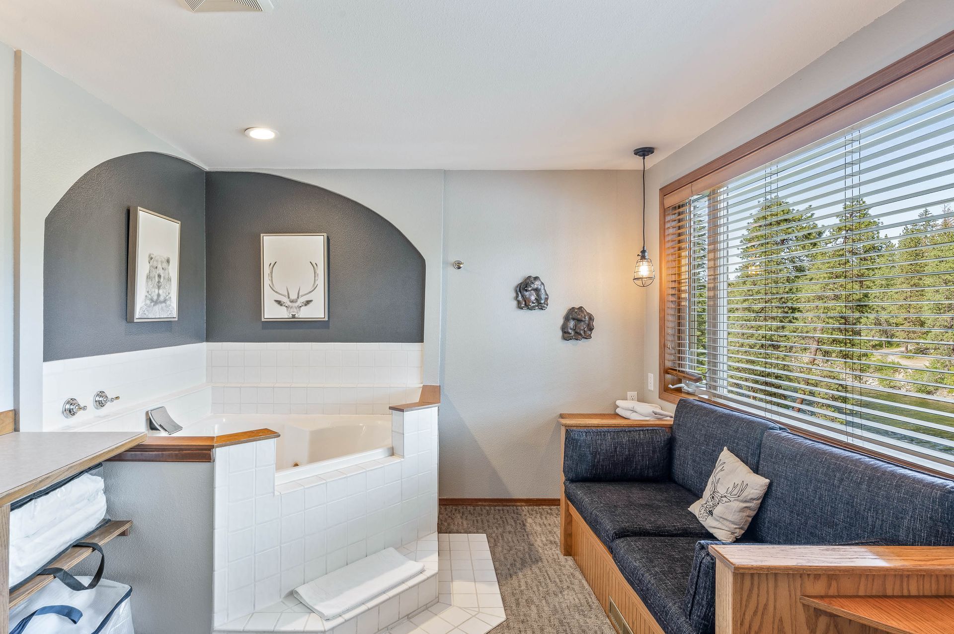 Bathroom with a jacuzzi tub, gray accent wall, built-in sofa, and window with blinds.