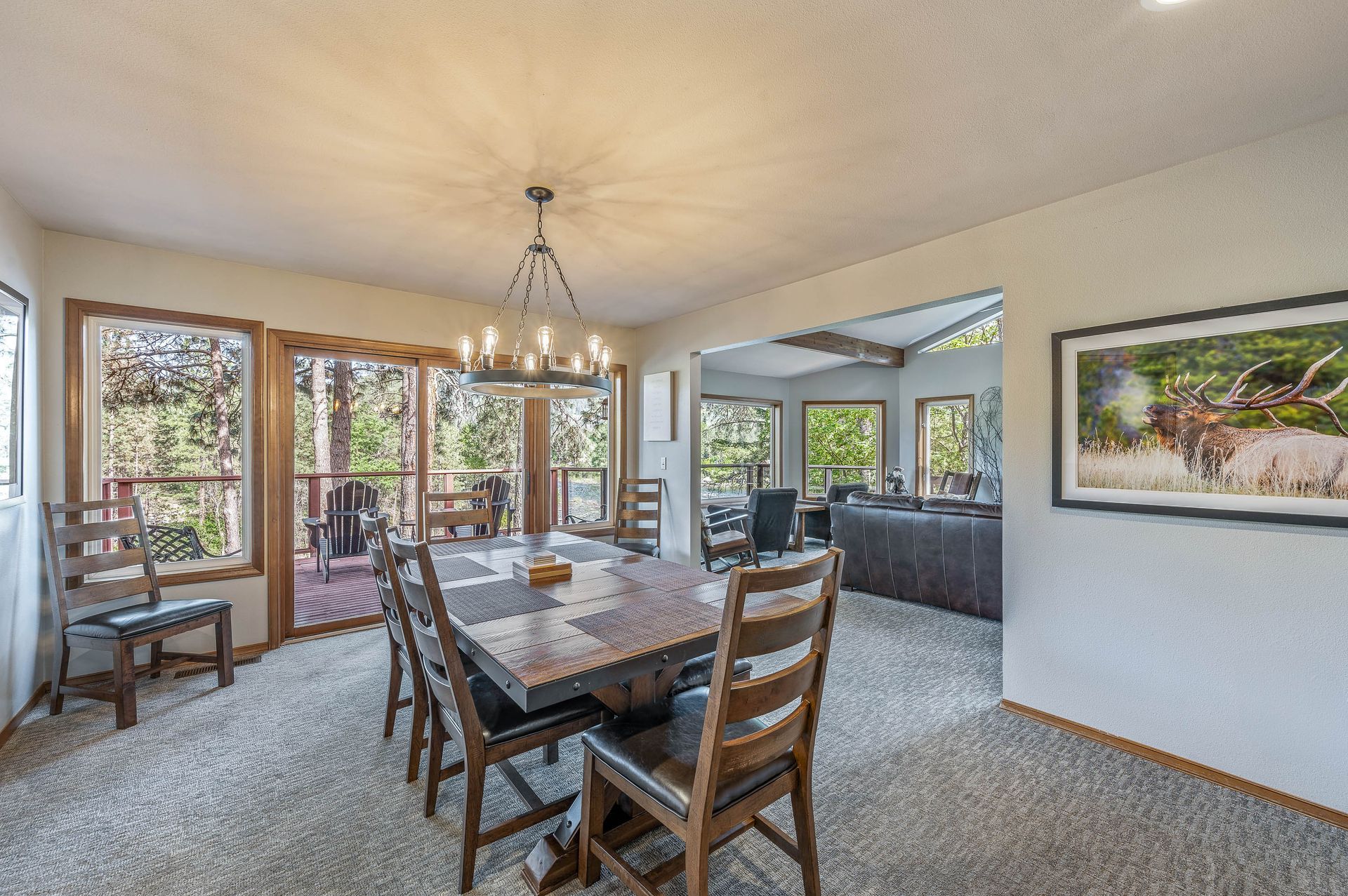 Dining room with wooden table and chairs, sliding door to deck, view of the living room, neutral colors, natural light.