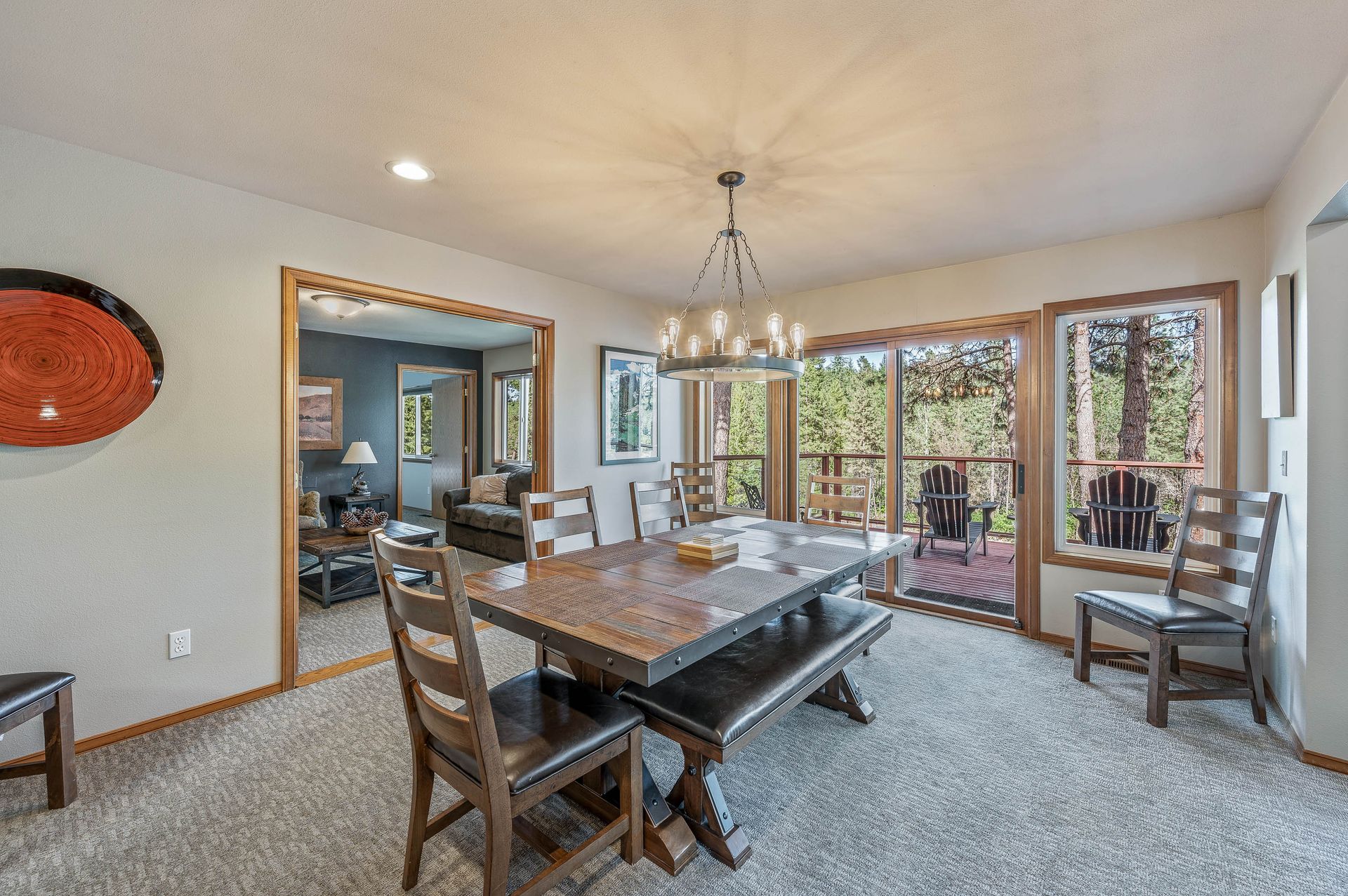 Dining room with large wood table, chairs, and bench, next to sliding glass doors with outdoor view.